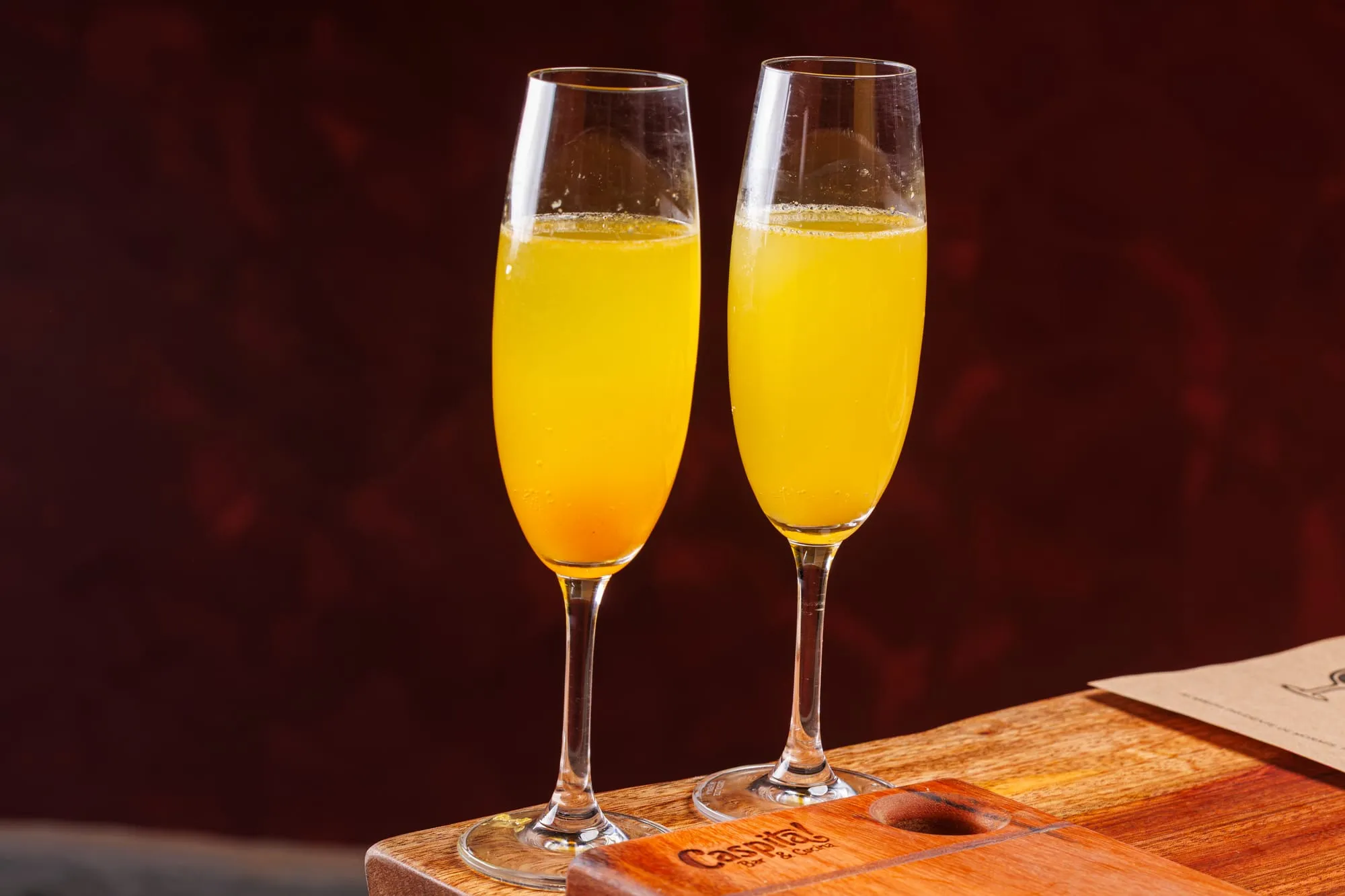 Duas taças de Bellini prontas para o brinde, contra a parede vermelha do bar
