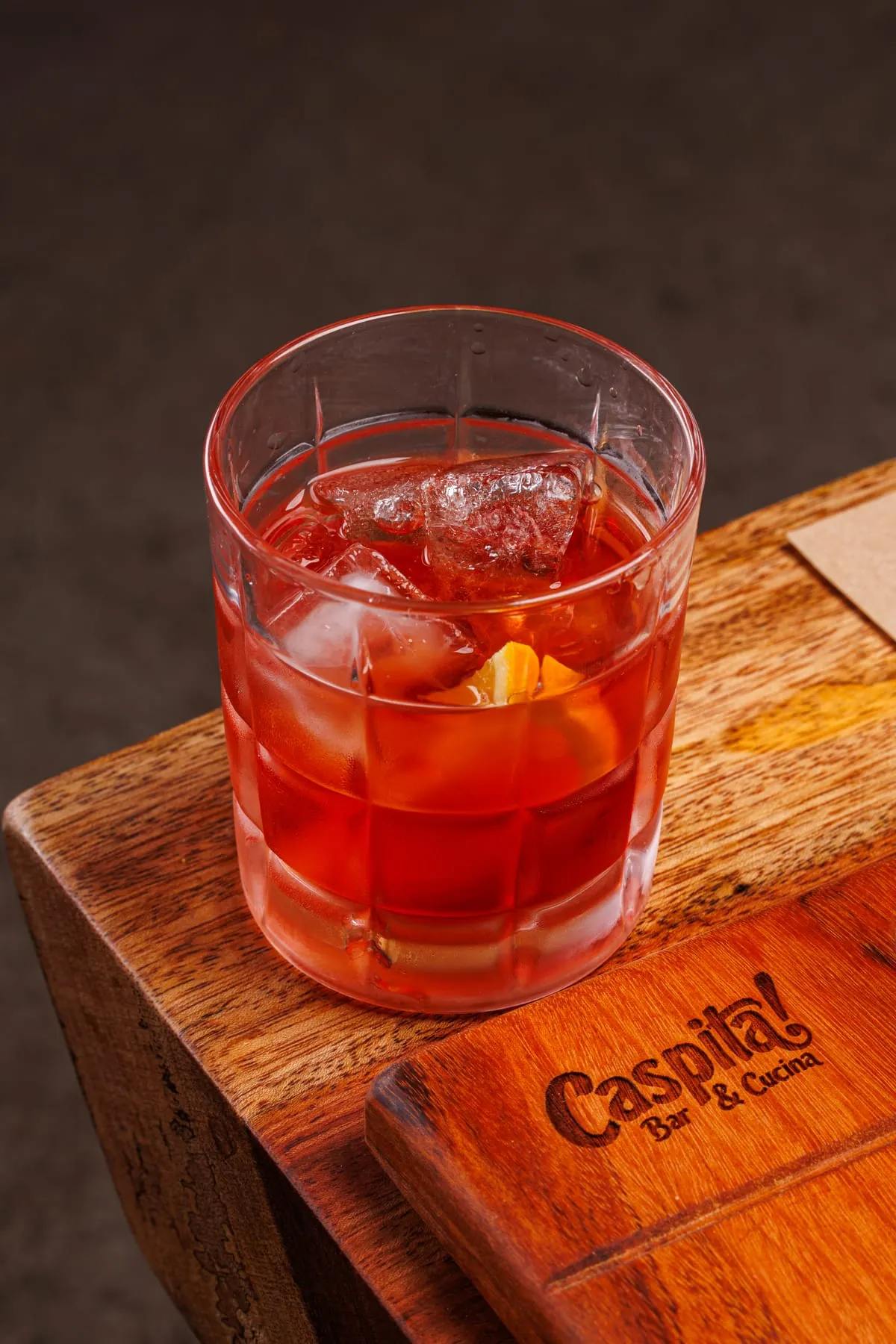 Negroni servido em copo baixo sobre tábua com a marca Caspita